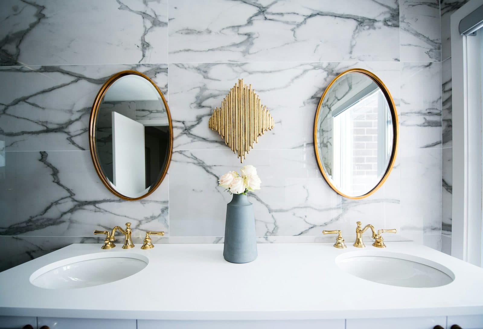 Dual-sink vanity in front of a bold white-and-gray veined marble feature wall with brass fixtures