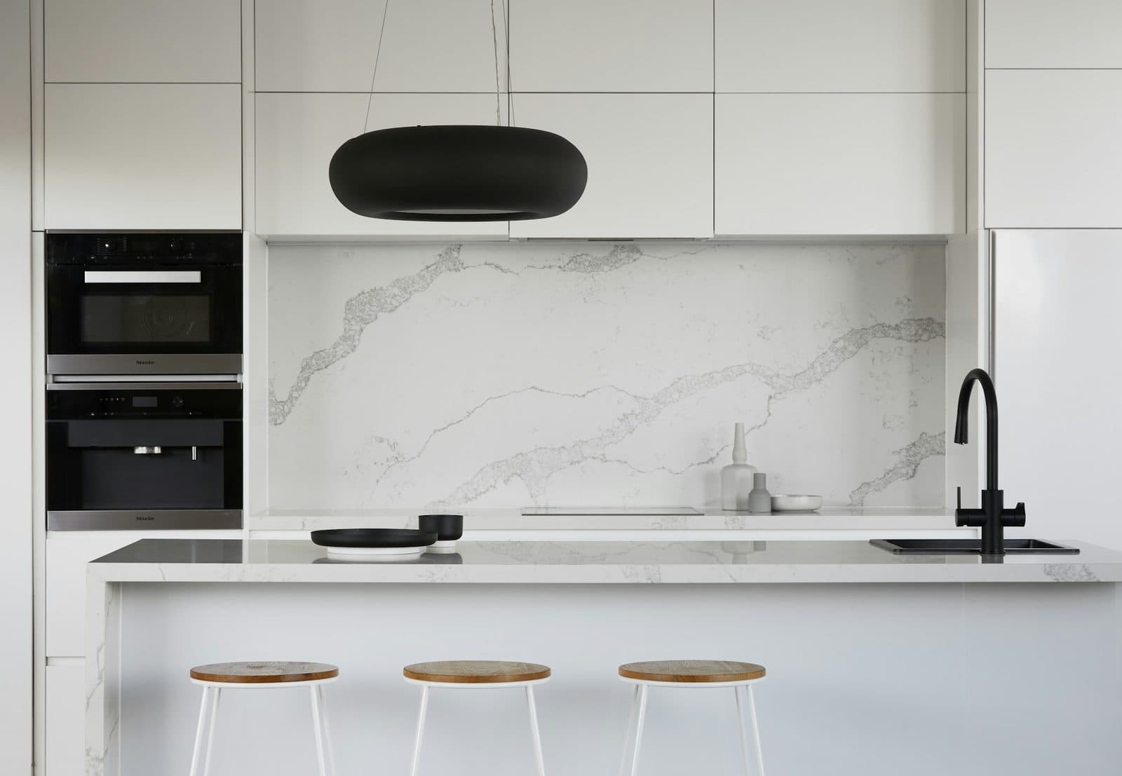 White veined stone slab backsplash behind a flush cooktop with a matching waterfall island
