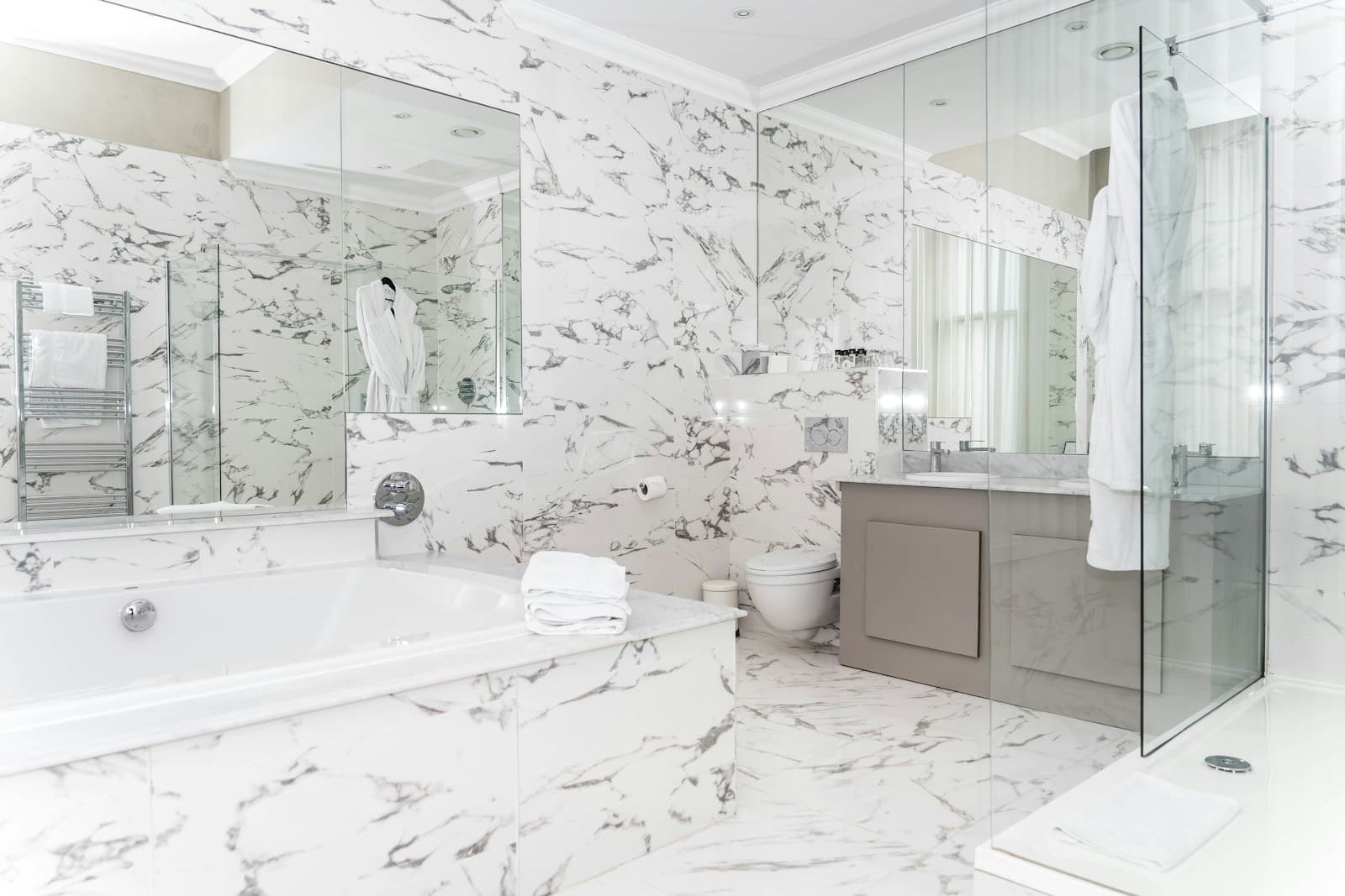 Luxury spa bathroom wrapped in white marble with built-in tub, vanity, and glass shower